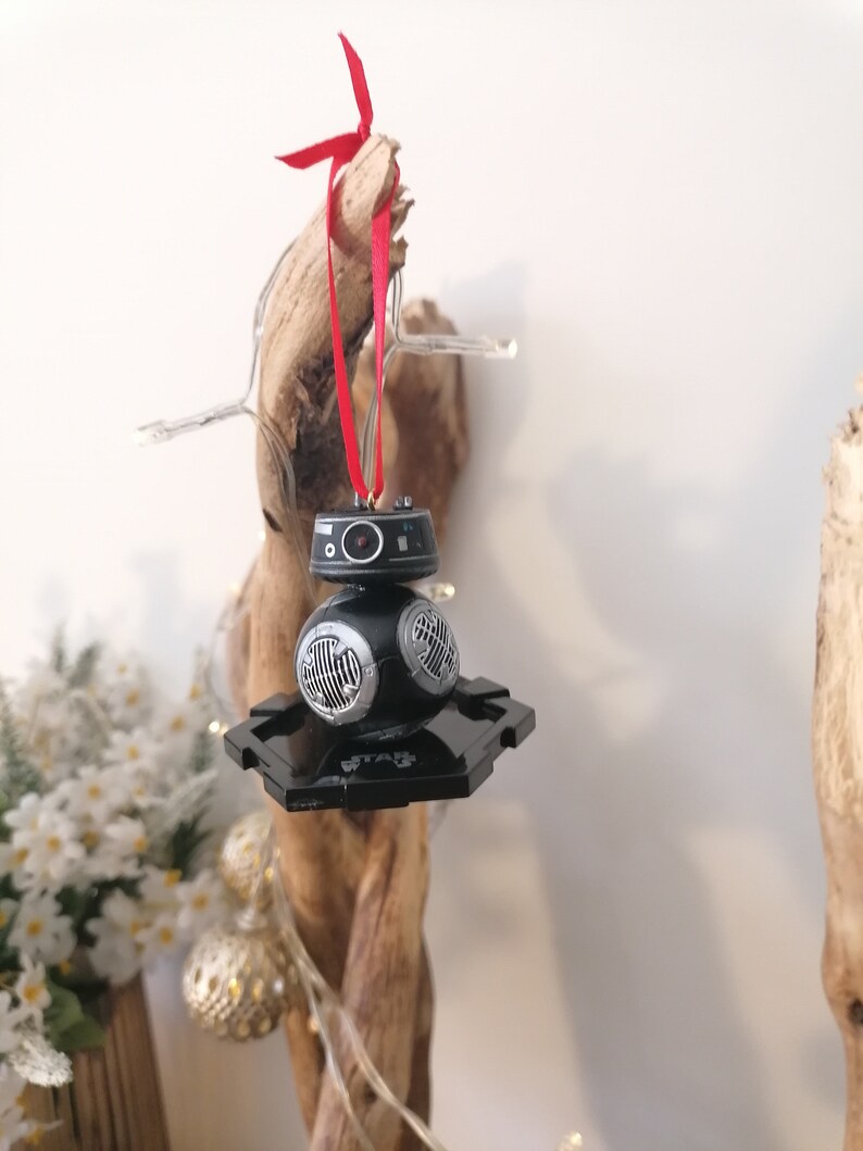 K&ouml;nnte beinhalten: Schwarzer und silberner Star Wars BB-8 Weihnachtsbaumschmuck mit einem roten Band, das an einem St&uuml;ck Treibholz h&auml;ngt.