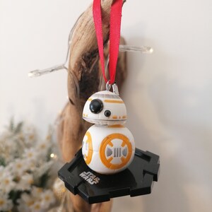 May include: A white and orange Star Wars BB-8 droid Christmas ornament with a black base and a red ribbon.