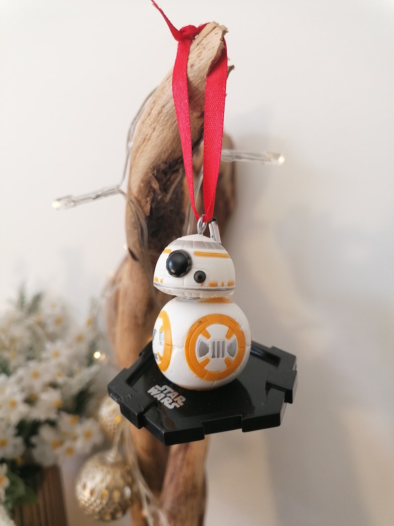 May include: A white and orange Star Wars BB-8 droid Christmas ornament with a black base and a red ribbon.