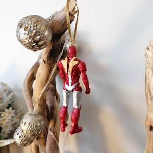 Pode incluir: Ornamento de Natal Iron Man vermelho e prateado pendurado em um galho com uma corda dourada.