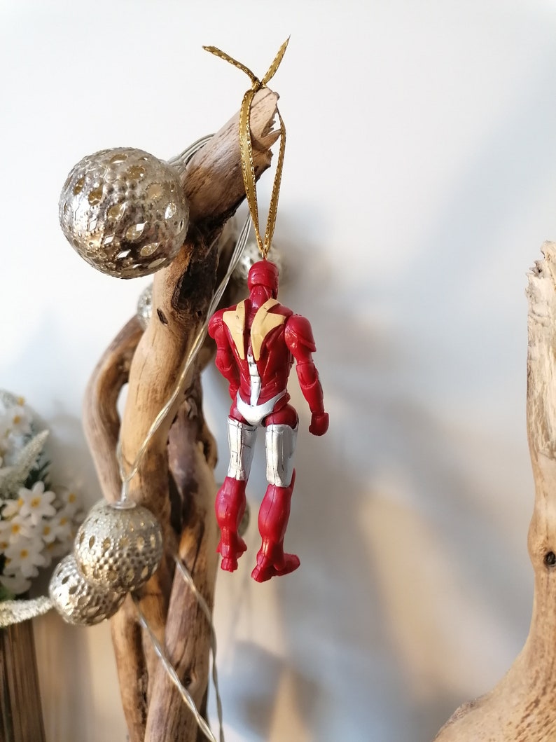 Pode incluir: Ornamento de Natal Iron Man vermelho e prateado pendurado em um galho com uma corda dourada.