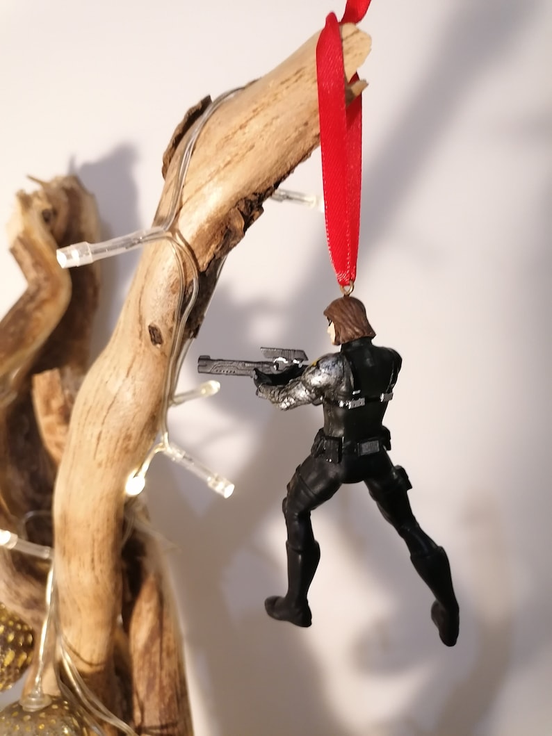 May include: A black and silver action figure of a superhero holding a gun, hanging from a red ribbon. The figure is wearing a black suit with silver accents and a black helmet. The figure is posed in a dynamic action pose.