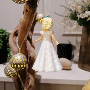 Peut inclure: Une figurine de poup&eacute;e en porcelaine blanche avec des cheveux blonds et une robe blanche. La poup&eacute;e est suspendue &agrave; une ficelle et est d&eacute;cor&eacute;e d'un n&oelig;ud bleu clair.