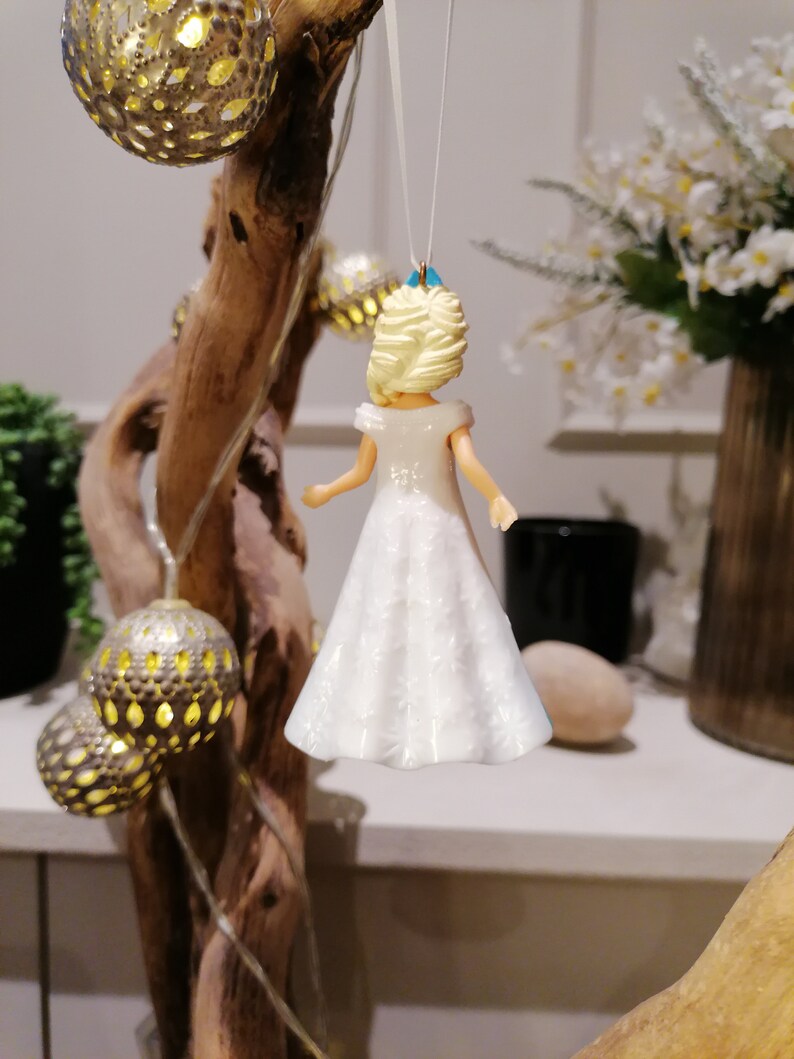 Peut inclure: Une figurine de poup&eacute;e en porcelaine blanche avec des cheveux blonds et une robe blanche. La poup&eacute;e est suspendue &agrave; une ficelle et est d&eacute;cor&eacute;e d'un n&oelig;ud bleu clair.