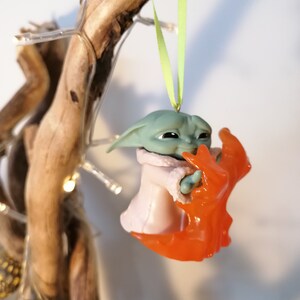 May include: A green and orange Christmas bauble featuring a character from the Star Wars franchise. The character is holding a small orange object in its hand.