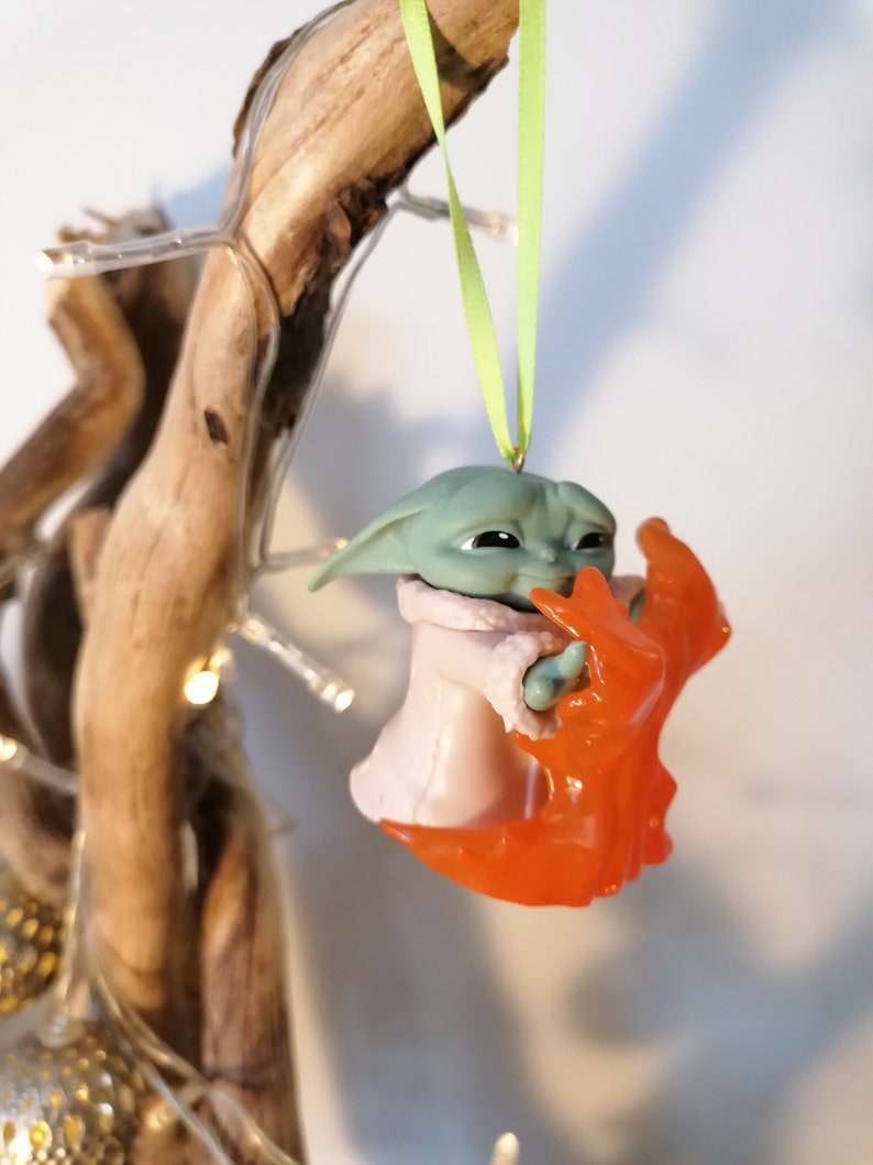 May include: A green and orange Christmas bauble featuring a character from the Star Wars franchise. The character is holding a small orange object in its hand.