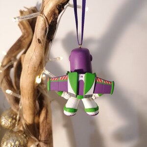 K&ouml;nnte beinhalten: Lila-gr&uuml;ner Weihnachtsbaumschmuck aus Plastik von Buzz Lightyear aus Toy Story, mit einem lila-wei&szlig;en Weltraum-Ranger-Anzug und Fl&uuml;geln, der an einem lila Band h&auml;ngt.