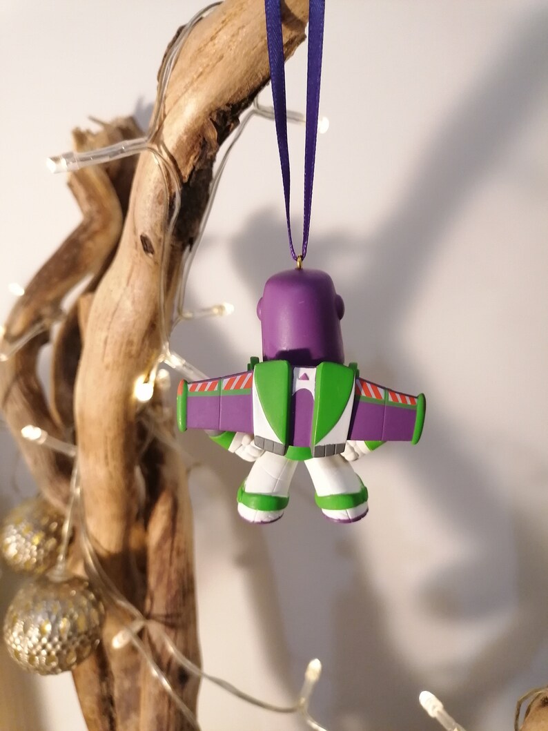 K&ouml;nnte beinhalten: Lila-gr&uuml;ner Weihnachtsbaumschmuck aus Plastik von Buzz Lightyear aus Toy Story, mit einem lila-wei&szlig;en Weltraum-Ranger-Anzug und Fl&uuml;geln, der an einem lila Band h&auml;ngt.