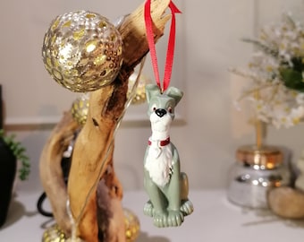 May include: A gray and white dog figurine ornament with a red collar hanging from a red ribbon on a driftwood branch with gold glitter ornaments.