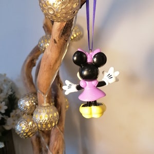 May include: Purple and black Minnie Mouse Christmas ornament hanging from a purple ribbon on a driftwood branch with silver and gold ornaments.