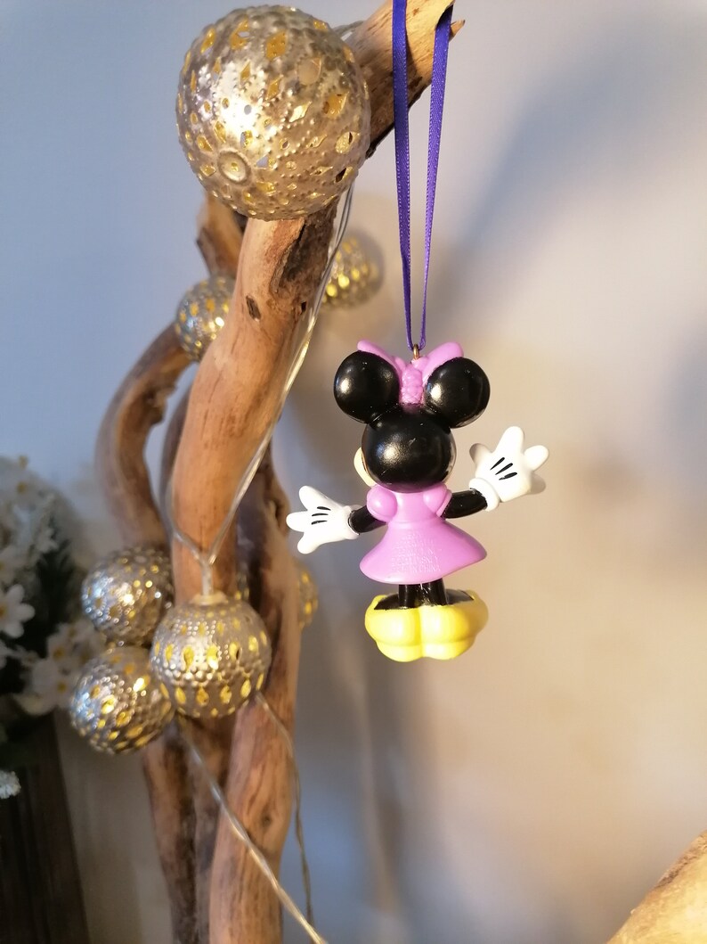 May include: Purple and black Minnie Mouse Christmas ornament hanging from a purple ribbon on a driftwood branch with silver and gold ornaments.