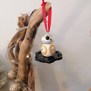 May include: A white and orange Star Wars BB-8 droid Christmas ornament with a black base and a red ribbon.