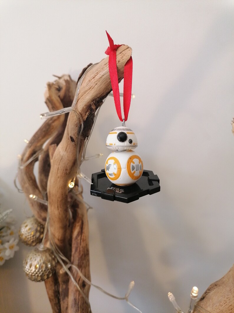 May include: A white and orange Star Wars BB-8 droid Christmas ornament with a black base and a red ribbon.