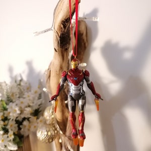 May include: Red and silver Iron Man Christmas ornament hanging from a piece of driftwood with a red ribbon.