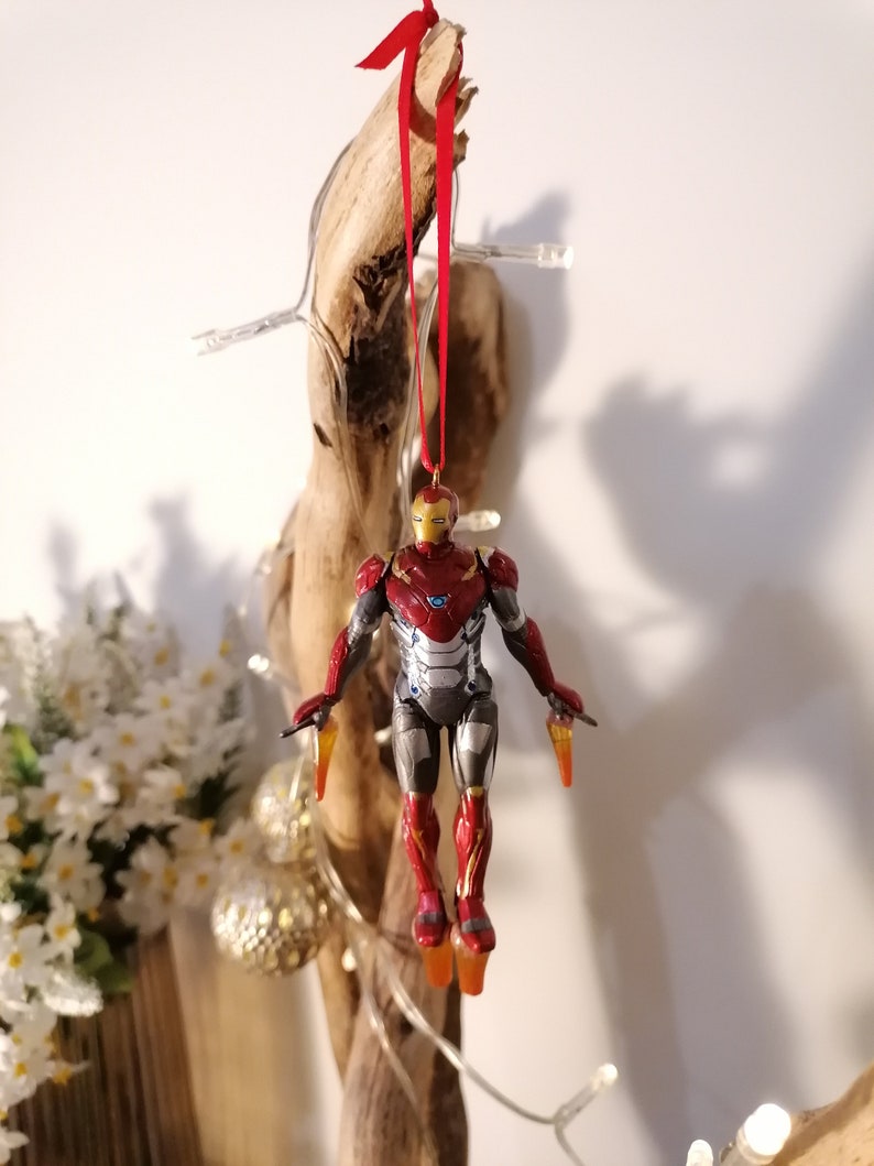 May include: Red and silver Iron Man Christmas ornament hanging from a piece of driftwood with a red ribbon.