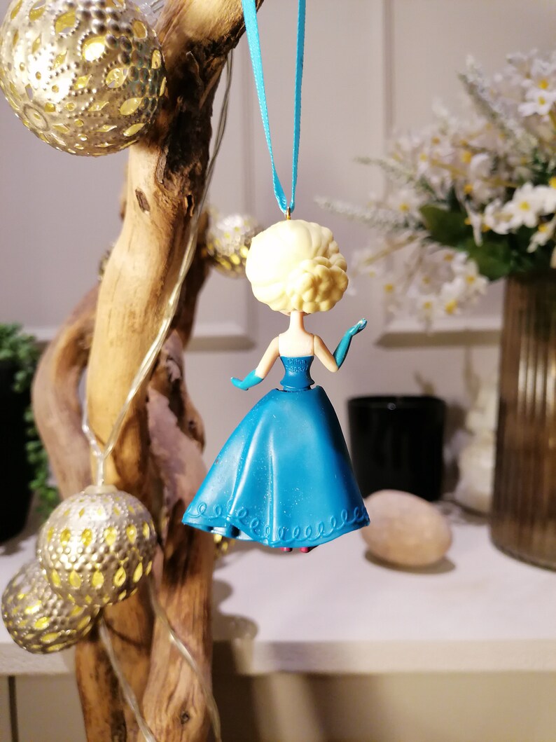 Peut inclure: Une d&eacute;coration de No&euml;l bleue et blanche repr&eacute;sentant une figurine de princesse v&ecirc;tue d'une robe bleue et d'une couronne blanche. La d&eacute;coration est suspendue &agrave; un ruban bleu.