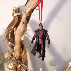 K&ouml;nnte beinhalten: Ein schwarzer und roter Star Wars-Charakter-Anh&auml;nger, der an einem Ast mit wei&szlig;en Lichtern h&auml;ngt. Der Charakter tr&auml;gt einen schwarzen Umhang und h&auml;lt einen Blaster.