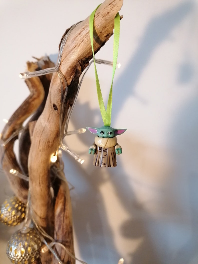 Puede incluir: Una figurita verde y marr&oacute;n de un personaje de la franquicia Star Wars, colgando de una cinta verde en un trozo de madera a la deriva.