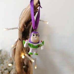 Puede incluir: Adorno navideño morado y verde con un personaje de dibujos animados de Buzz Lightyear de la franquicia de películas Toy Story.