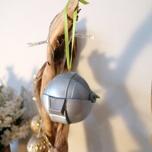 May include: A silver and green Christmas ornament shaped like a spaceship, hanging from a branch with a green ribbon.