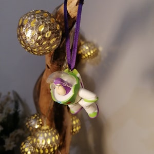 May include: A purple and green toy astronaut ornament hanging from a branch with gold and silver ornaments.