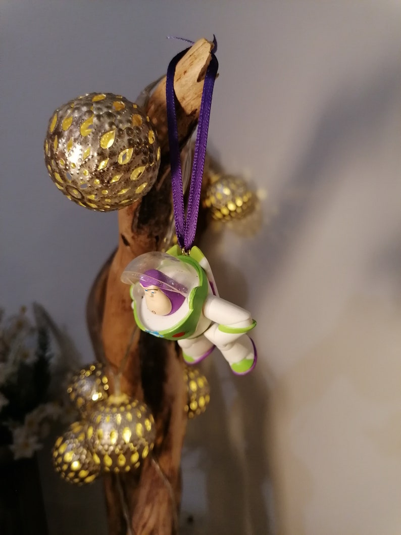 May include: A purple and green toy astronaut ornament hanging from a branch with gold and silver ornaments.