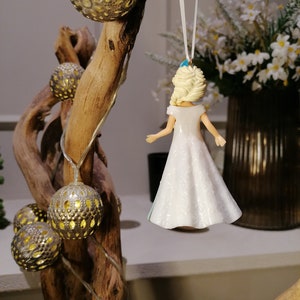 Peut inclure: Une figurine en porcelaine blanche repr&eacute;sentant une femme aux cheveux blonds portant une robe blanche. La figurine est suspendue &agrave; une ficelle blanche et est d&eacute;cor&eacute;e d'accents bleus.