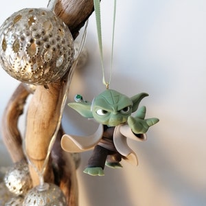 May include: A green Yoda ornament with a white robe and a green lightsaber hanging from a green ribbon.