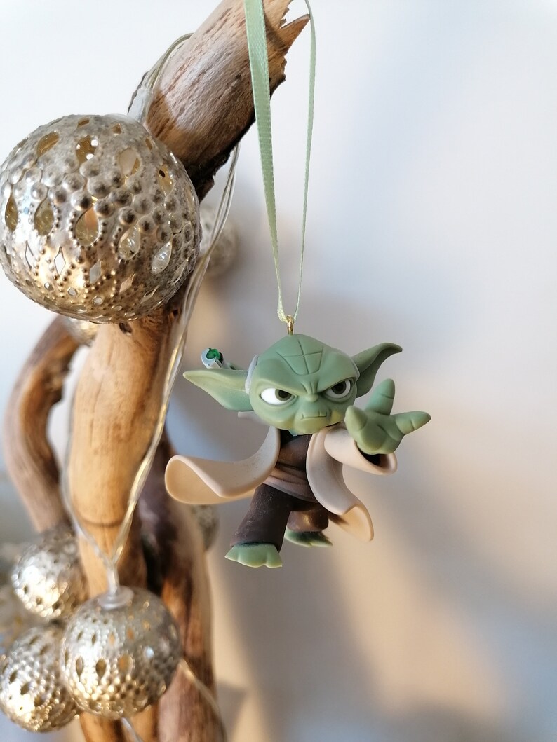 May include: A green Yoda ornament with a white robe and a green lightsaber hanging from a green ribbon.