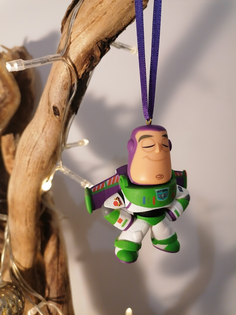 K&ouml;nnte beinhalten: Ein gr&uuml;ner und lila Buzz Lightyear Weihnachtsbaumschmuck mit einem lila Band. Der Schmuck ist eine stilisierte Version des Charakters aus den Toy Story Filmen.