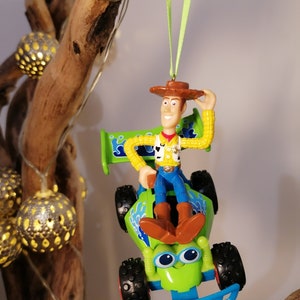 May include: A green toy race car with a blue bumper and a blue and green design.  Woody from Toy Story is sitting in the driver's seat, wearing his signature cowboy hat and vest.  The car is hanging from a green ribbon.