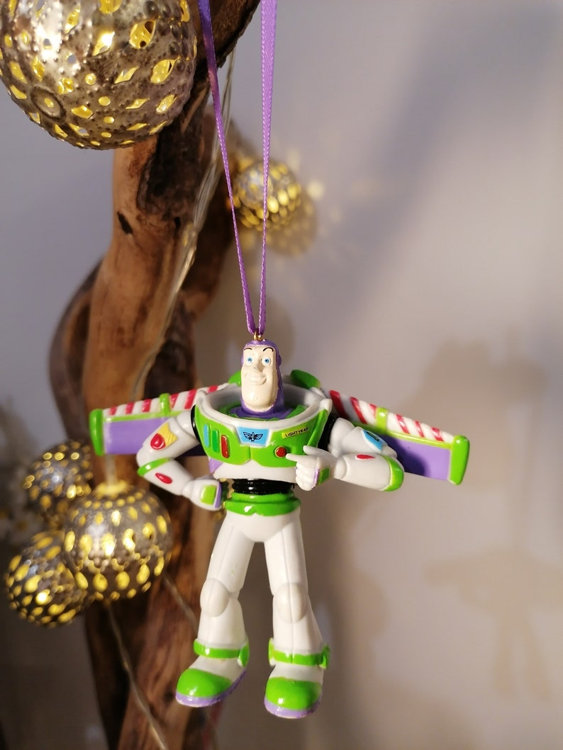 Peut inclure: Ornement de No&euml;l Buzz l'&Eacute;clair, avec une combinaison spatiale blanche et verte et des d&eacute;tails violets. Le soldat jouet est suspendu &agrave; un ruban violet. D&eacute;coration festive.