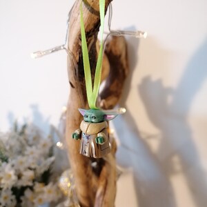 Puede incluir: Una figurita verde y marr&oacute;n de un personaje de la franquicia Star Wars, colgando de una cinta verde en un trozo de madera a la deriva.