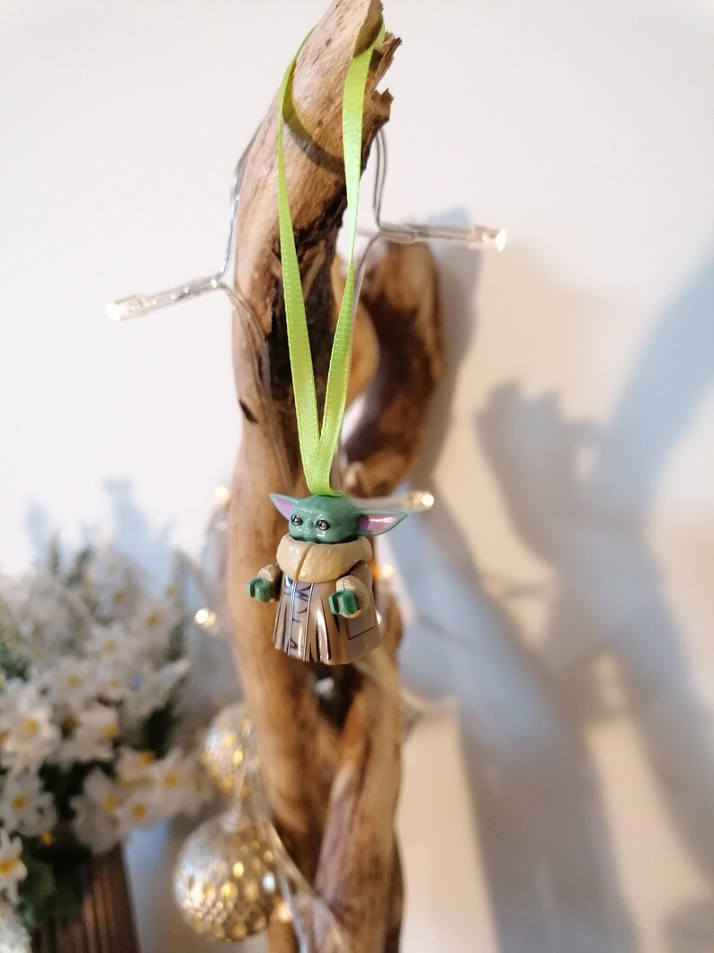 Puede incluir: Una figurita verde y marr&oacute;n de un personaje de la franquicia Star Wars, colgando de una cinta verde en un trozo de madera a la deriva.