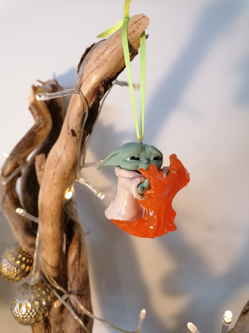 May include: A green and orange Christmas bauble featuring a character from the Star Wars franchise. The character is holding a small orange object in its hands.