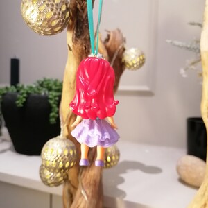 Peut inclure: Une figurine de poup&eacute;e aux cheveux roux et v&ecirc;tue de violet suspendue &agrave; une branche avec un ruban turquoise.