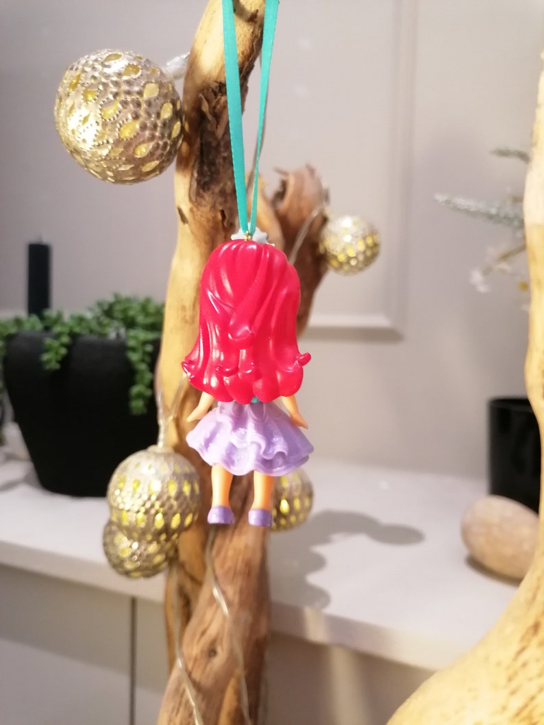 Peut inclure: Une figurine de poup&eacute;e aux cheveux roux et v&ecirc;tue de violet suspendue &agrave; une branche avec un ruban turquoise.