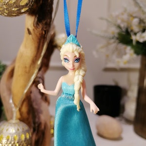 K&ouml;nnte beinhalten: Ein blauer und wei&szlig;er Plastik-Anh&auml;nger einer Disney-Prinzessin mit langen blonden Haaren, die ein blaues Kleid und eine Krone tr&auml;gt.