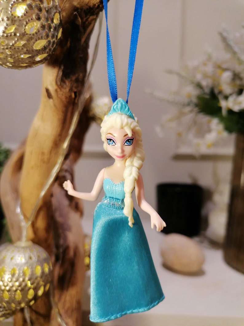 K&ouml;nnte beinhalten: Ein blauer und wei&szlig;er Plastik-Anh&auml;nger einer Disney-Prinzessin mit langen blonden Haaren, die ein blaues Kleid und eine Krone tr&auml;gt.