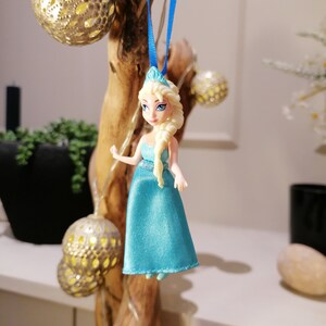 K&ouml;nnte beinhalten: Eine blaue und wei&szlig;e Plastikpuppe einer Prinzessin in einem blauen Kleid und einer Krone. Die Puppe h&auml;ngt an einem blauen Band.