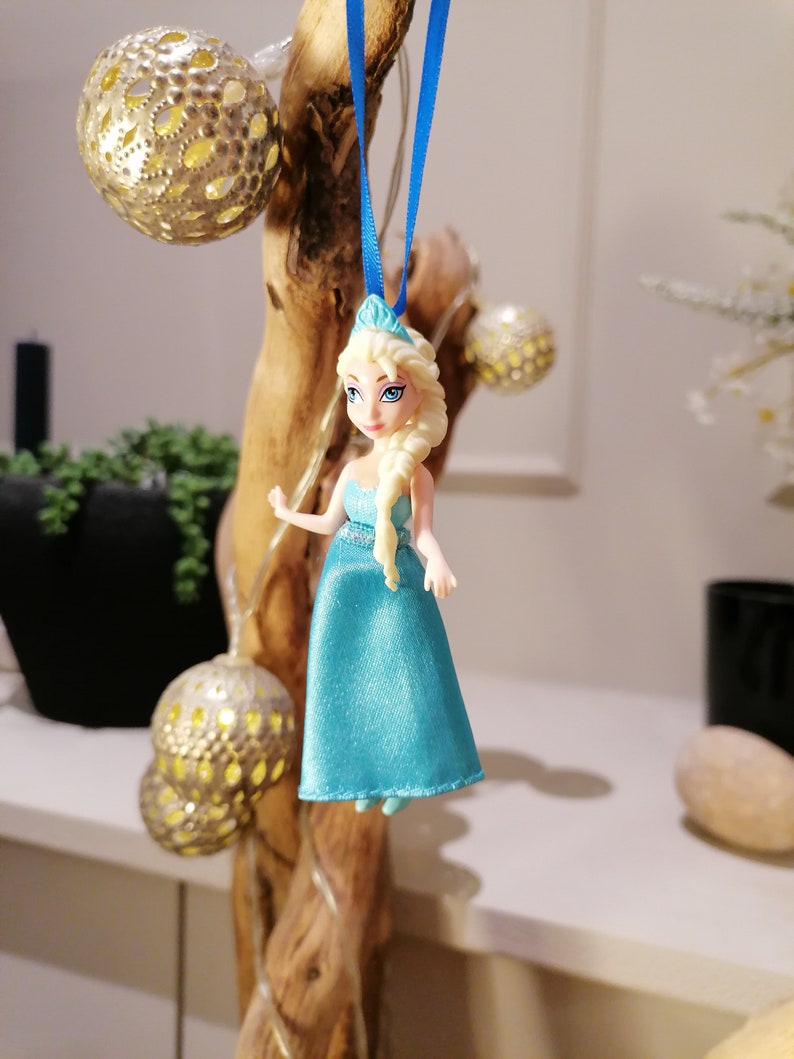 K&ouml;nnte beinhalten: Eine blaue und wei&szlig;e Plastikpuppe einer Prinzessin in einem blauen Kleid und einer Krone. Die Puppe h&auml;ngt an einem blauen Band.