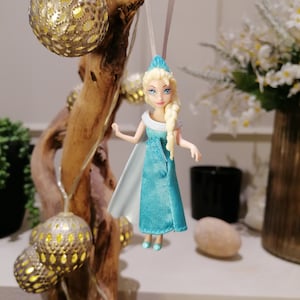 May include: A blue and white doll with blonde hair and a crown hanging from a branch with gold ornaments.