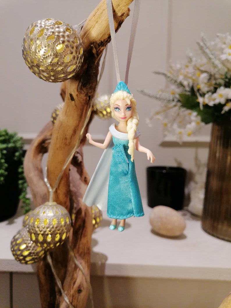 May include: A blue and white doll with blonde hair and a crown hanging from a branch with gold ornaments.