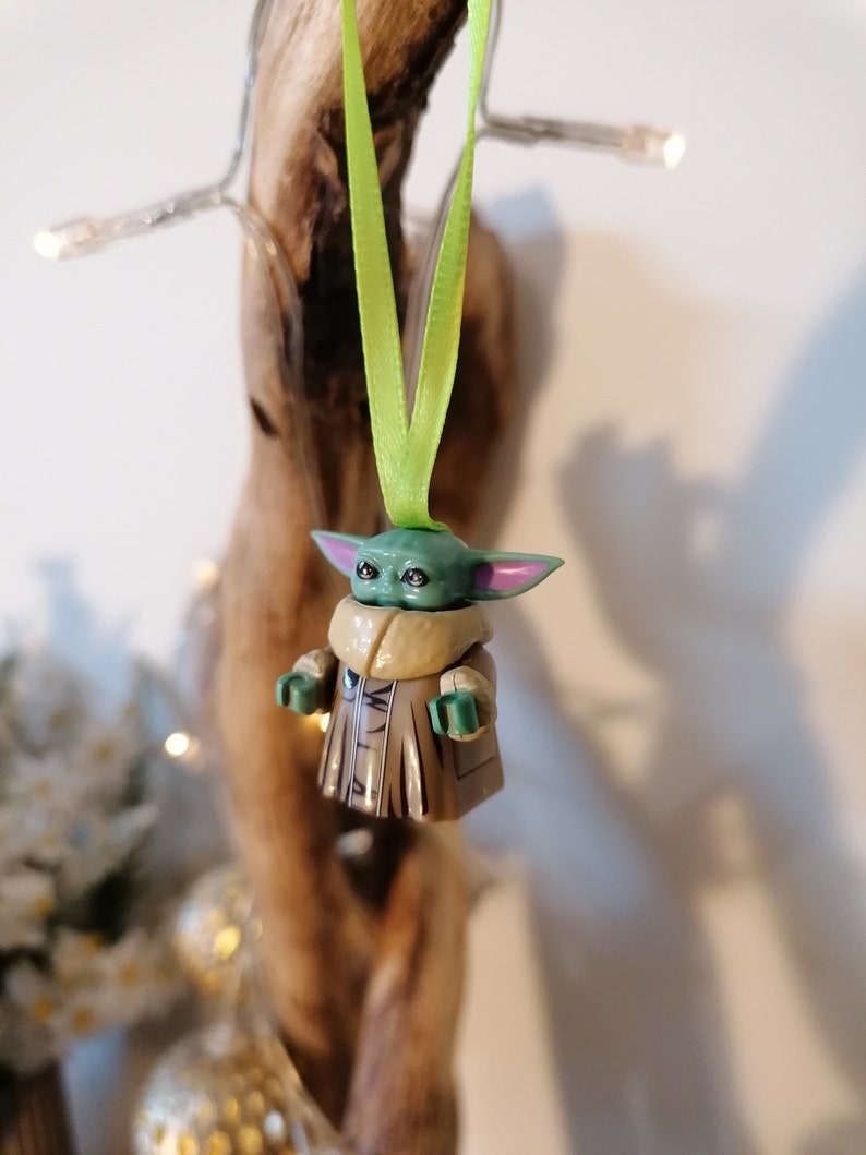 Puede incluir: Una figurita verde y marr&oacute;n de un personaje de la franquicia Star Wars, colgada de una cinta verde. La figurita lleva un abrigo marr&oacute;n y tiene orejas grandes.