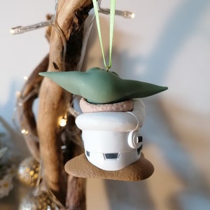 K&ouml;nnte beinhalten: Ein gr&uuml;ner und wei&szlig;er Weihnachtsbaumschmuck mit einer Figur aus dem Star Wars-Franchise. Der Schmuck ist in Form einer kleinen Person mit einer wei&szlig;en Kapuzenrobe und einem gr&uuml;nen Hut. Der Schmuck h&auml;ngt an einem gr&uuml;nen Band.
