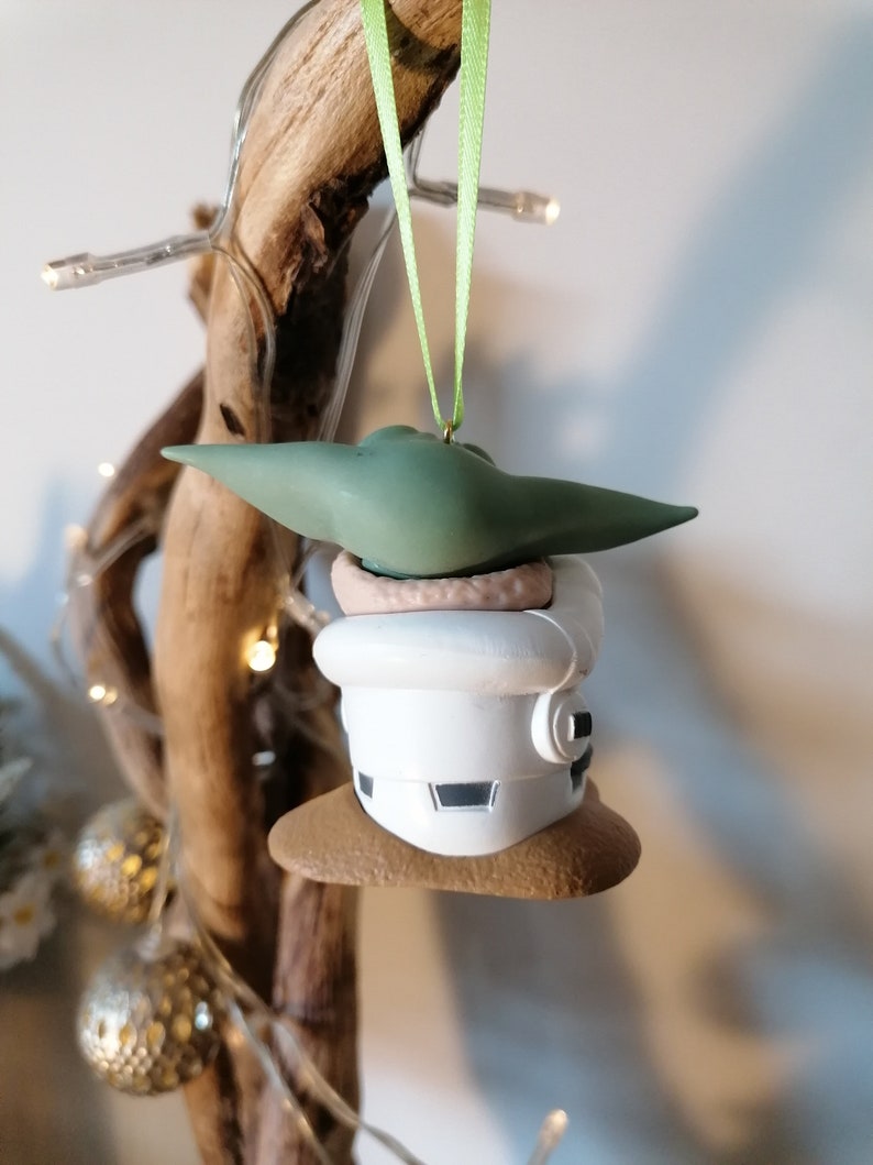 K&ouml;nnte beinhalten: Ein gr&uuml;ner und wei&szlig;er Weihnachtsbaumschmuck mit einer Figur aus dem Star Wars-Franchise. Der Schmuck ist in Form einer kleinen Person mit einer wei&szlig;en Kapuzenrobe und einem gr&uuml;nen Hut. Der Schmuck h&auml;ngt an einem gr&uuml;nen Band.
