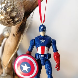 May include: A red, white, and blue Captain America action figure ornament with a red ribbon and a shield.