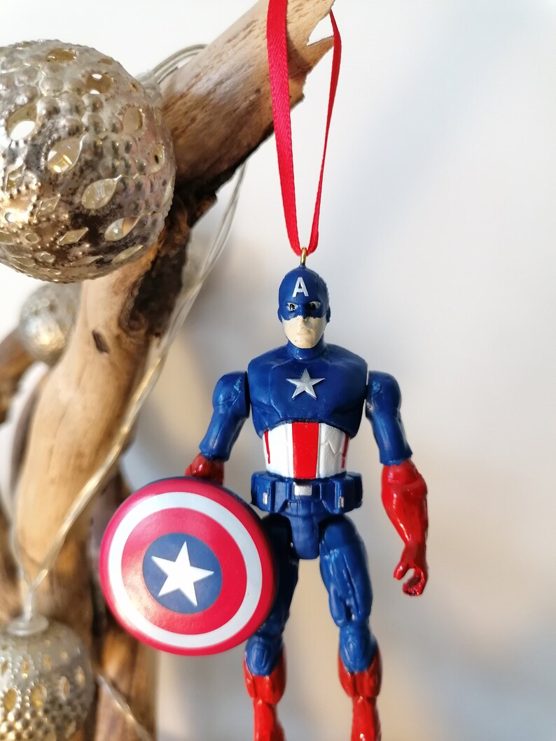 May include: A red, white, and blue Captain America action figure ornament with a red ribbon and a shield.