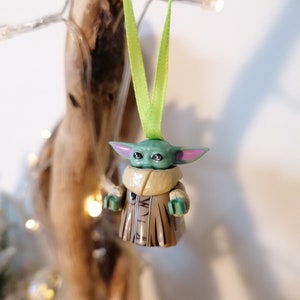 Puede incluir: Una figura de Lego verde y marr&oacute;n de un personaje de la franquicia Star Wars, colgada de una cinta verde. La figura lleva una t&uacute;nica marr&oacute;n y tiene orejas grandes.