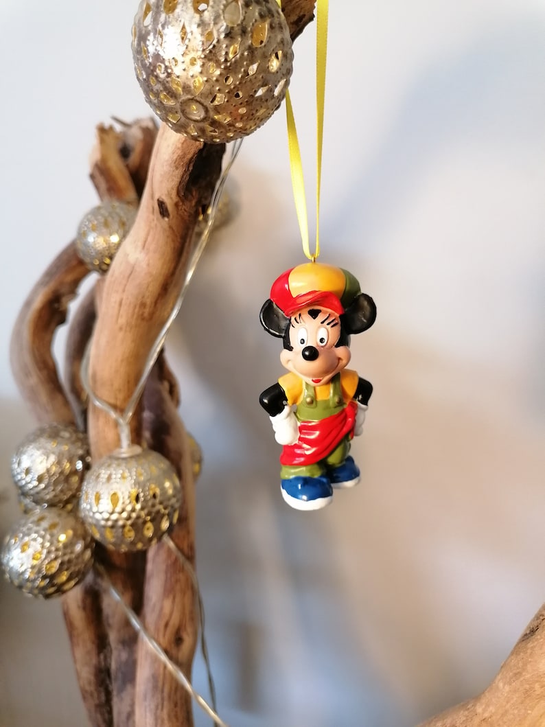 May include: A red, yellow and green Mickey Mouse ornament with a red hat and blue shoes. The ornament is hanging from a yellow ribbon.